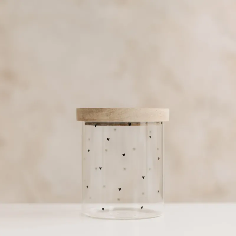 Leeres Vorratsglas mit kleinen schwarzen Herzen und aufgesetztem Holzdeckel vor hellem Hintergrund.