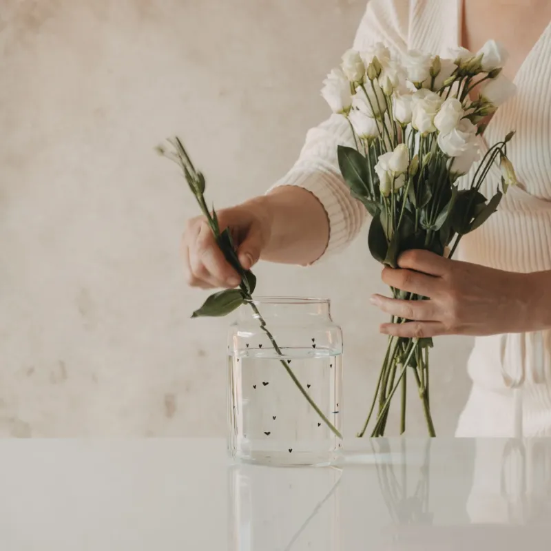 Glasvase mit schwarzen Herzen wird mit weißen Blumen bestückt
