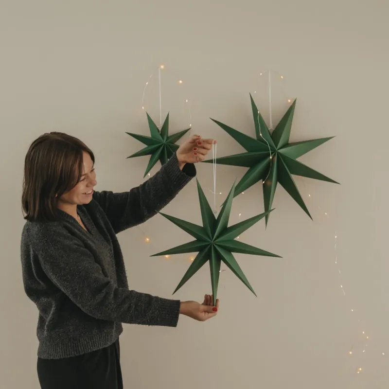 Drei dunkelgrüne Papiersterne mit Lichterkette, einer davon wird dekorativ in der Hand gehalten